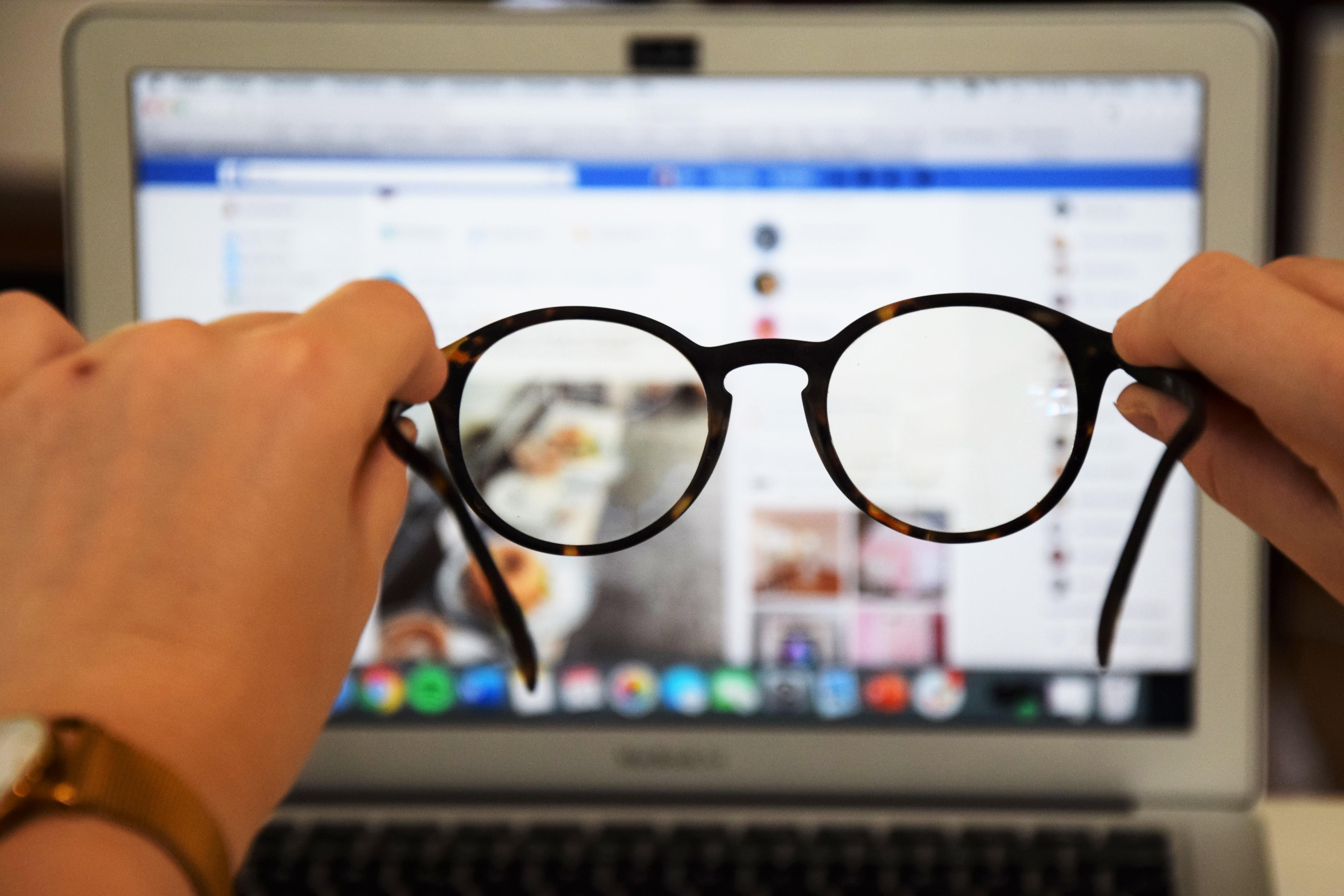 Durch eine Brille ist ein Laptop zu sehen, auf dem ein soziales Netzwerk geöffnet ist.